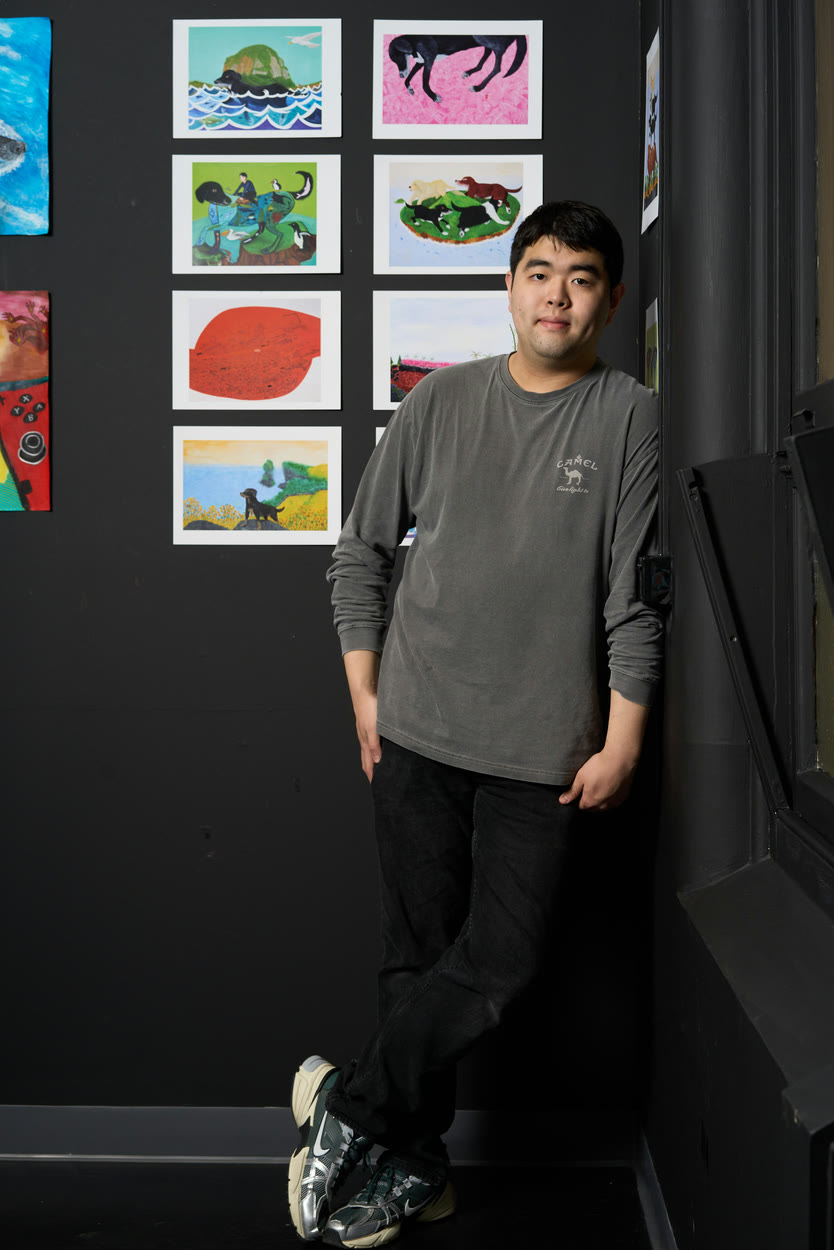 An artist standing beside a wall of small paintings