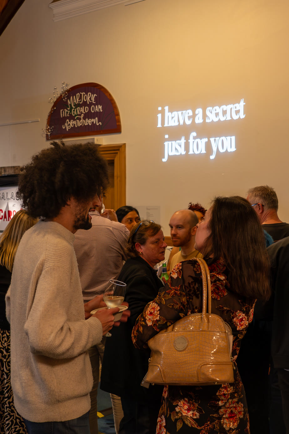 Visitors beneath a neon sign reading 'i have a secret just for you'